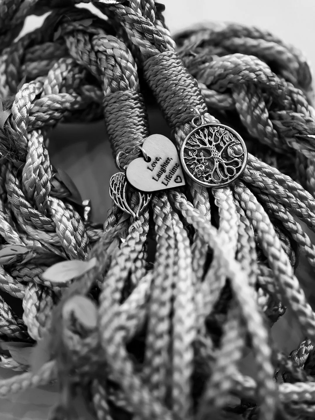 A pile of thick, woven ropes with three charms hanging from them: a heart-shaped charm engraved with the words 'Love, Laughter, Lifting'; a leaf-shaped charm; and a circular charm with a tree design.