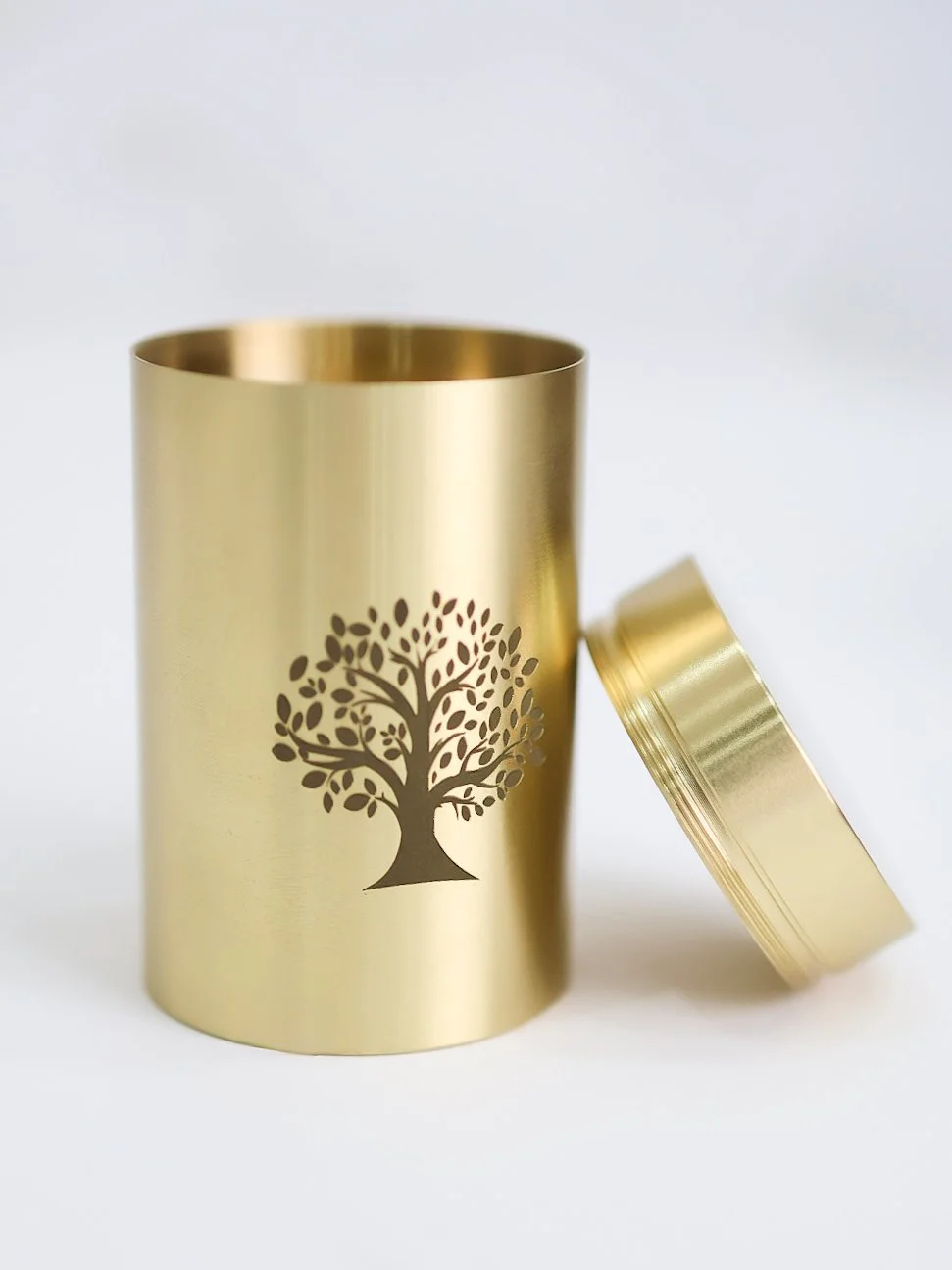 A gold-colored cylindrical container with a lid, featuring a tree silhouette design on its surface.