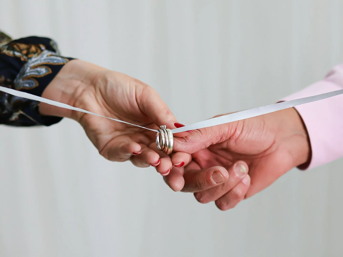 Two people are exchanging wedding rings on a white ribbon during a ceremony.