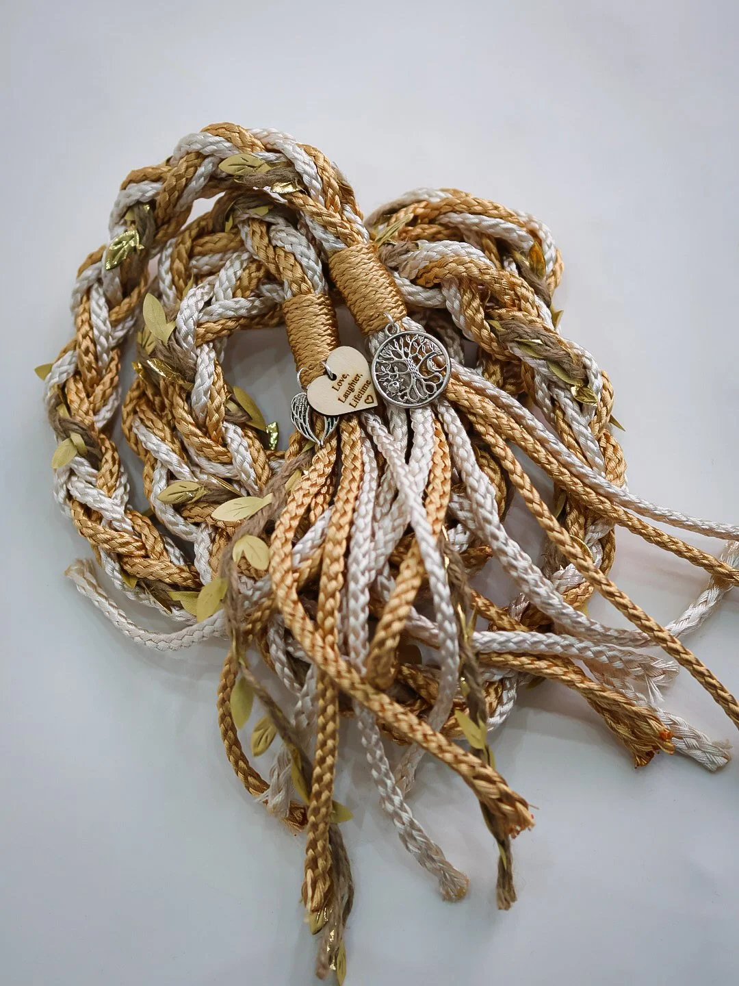 Bunch of braided cords in gold and white with metal charms and leaf decorations.