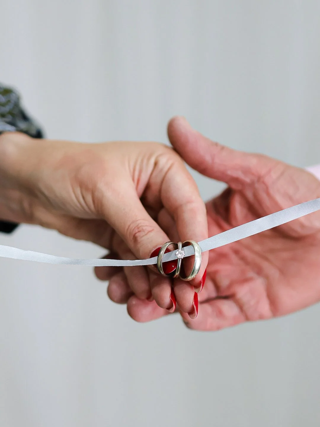 Two women hold wedding rings and cut a white ribbon, symbolizing an engagement or wedding ceremony.