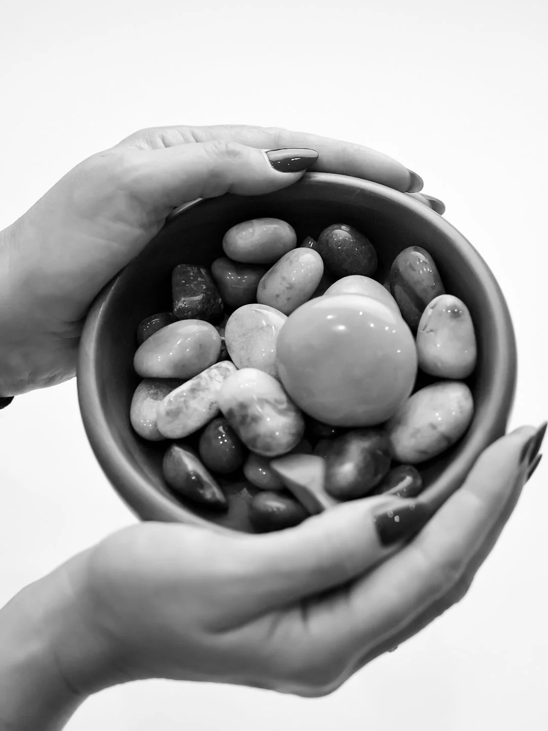 Black and white photo of hands holding a bowl filled with smooth, rounded stones