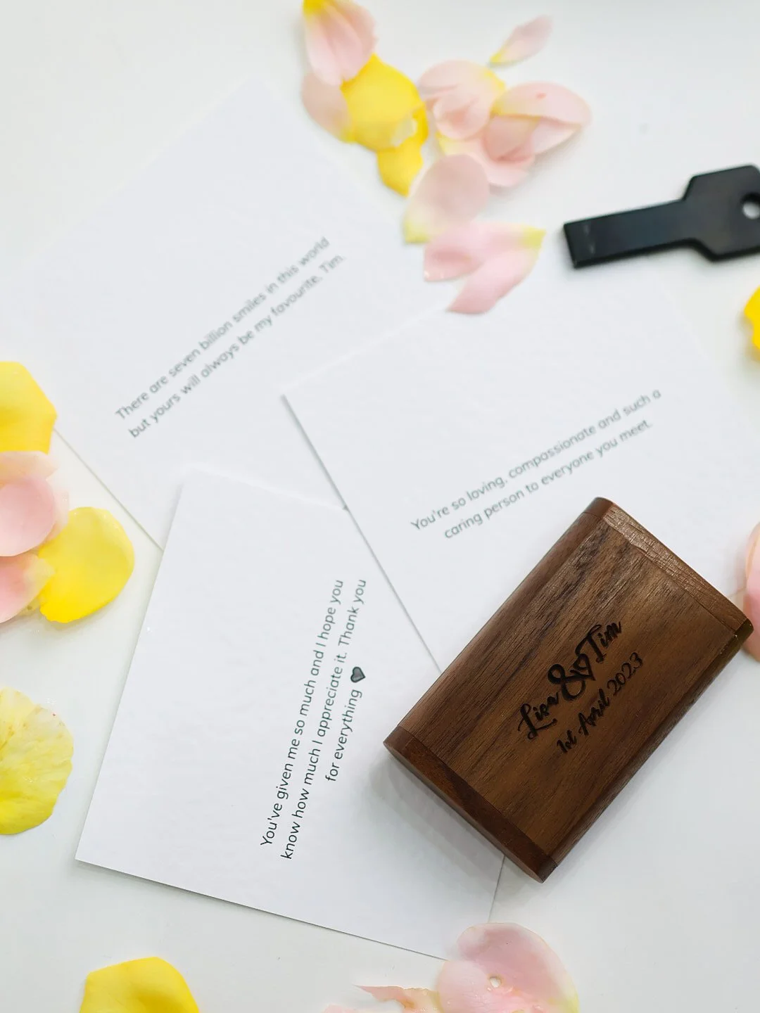 Letters of appreciation surrounded by pink and yellow flower petals, a black keychain, and a wooden stamp with the words 'Love & Team' and 'April 2023' engraved on it.