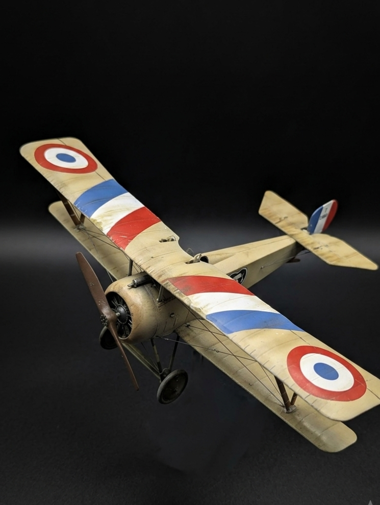 Model WWII airplane with a camouflage paint job, featuring red, white, and blue roundels, set against a black background.