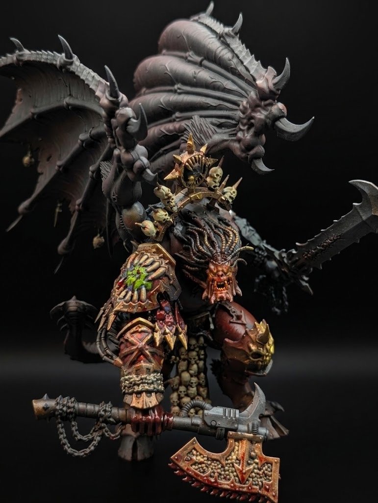 A detailed miniature figurine of a demonic warrior with armor decorated with skulls, wielding a large axe, and with large wings made of bones and spikes, set against a dark background.