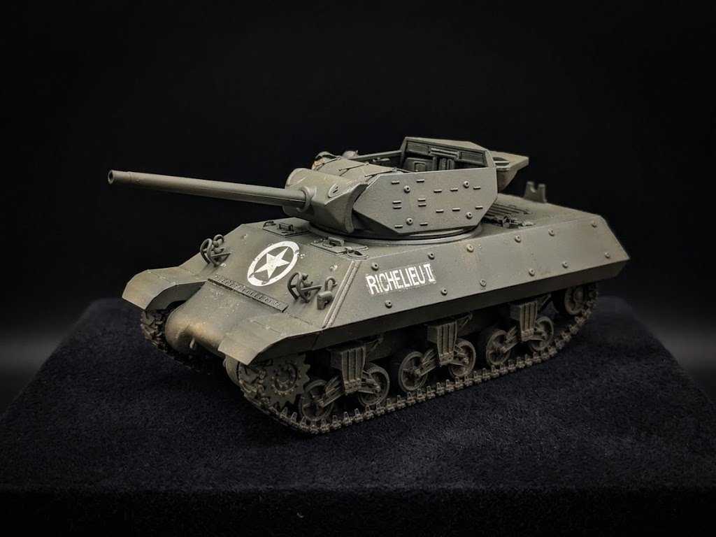 A model of a military tank with a long barrel, markings, and tracks, placed on a black surface against a black background.