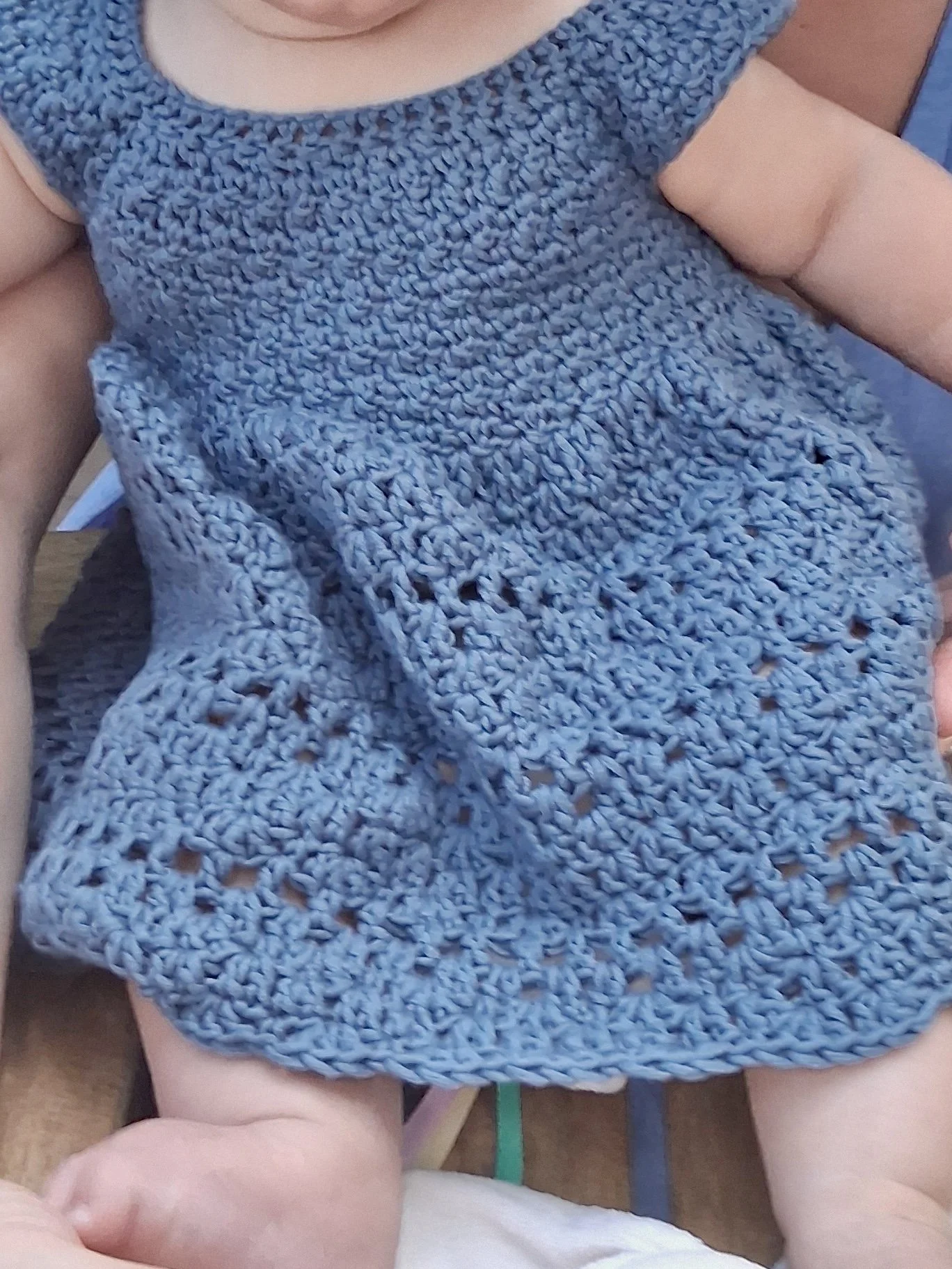 Close-up of a baby wearing a blue, crocheted dress by Tessa Smith Designs.