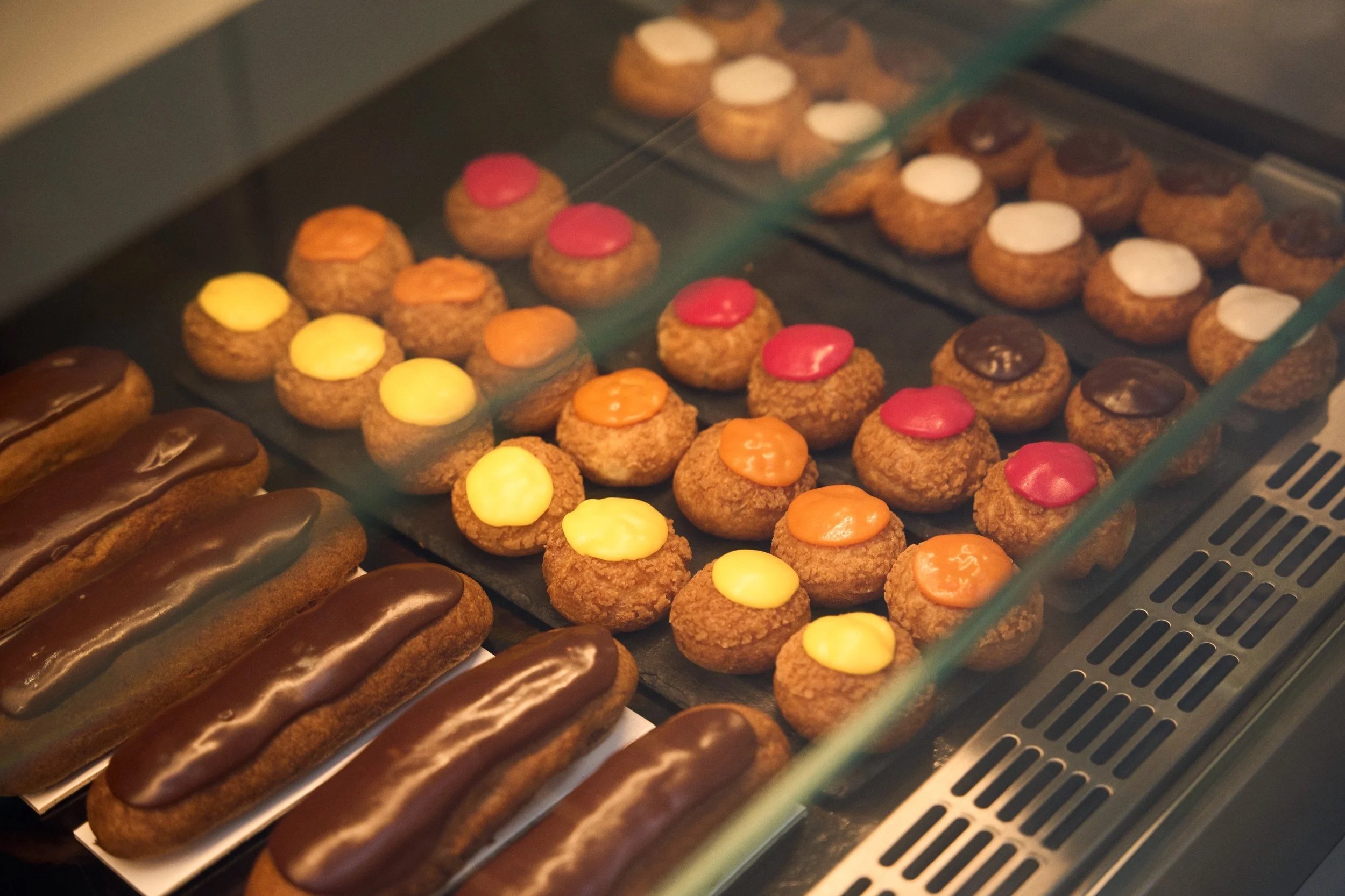 Colorful choux pastries and chocolate éclairs displayed in a Paris pastry shop