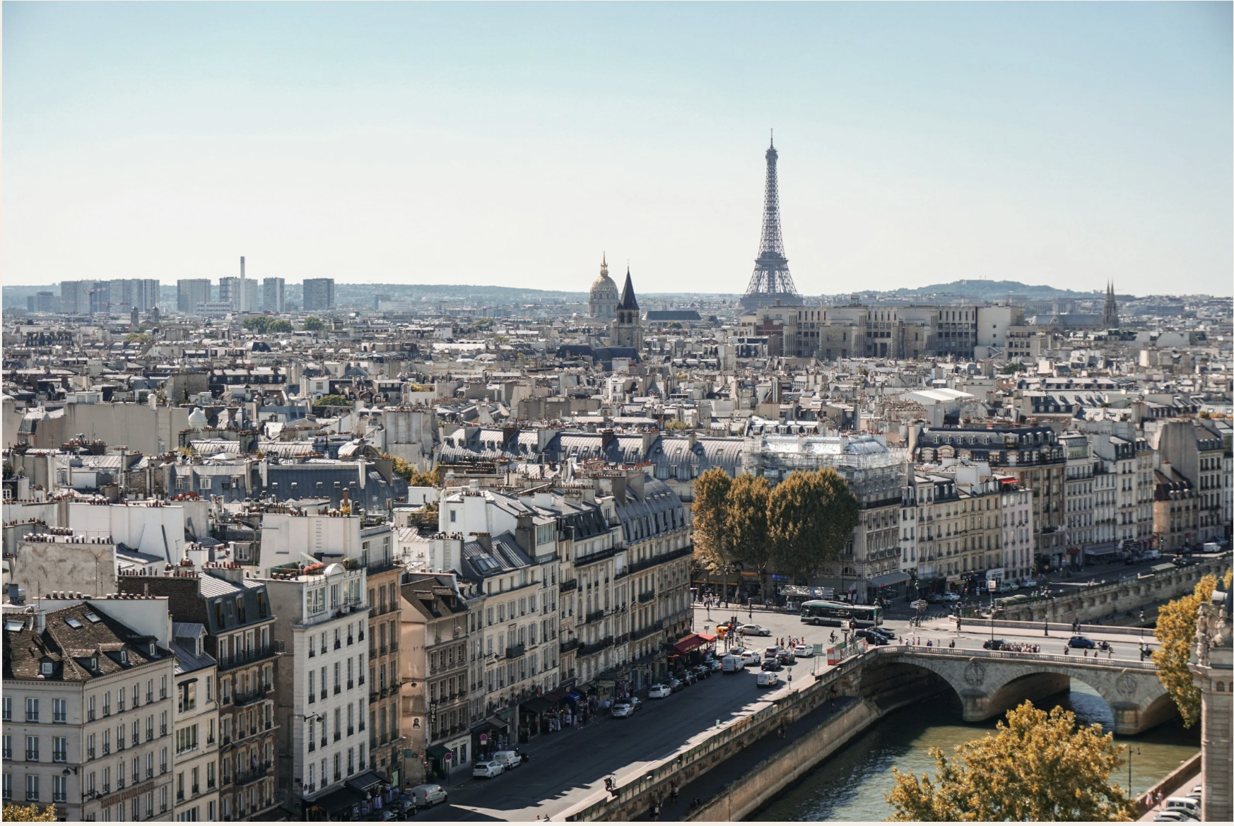 Panoramic view of Paris with the Eiffel Tower, the Seine River, historic rooftops, and a stone bridge