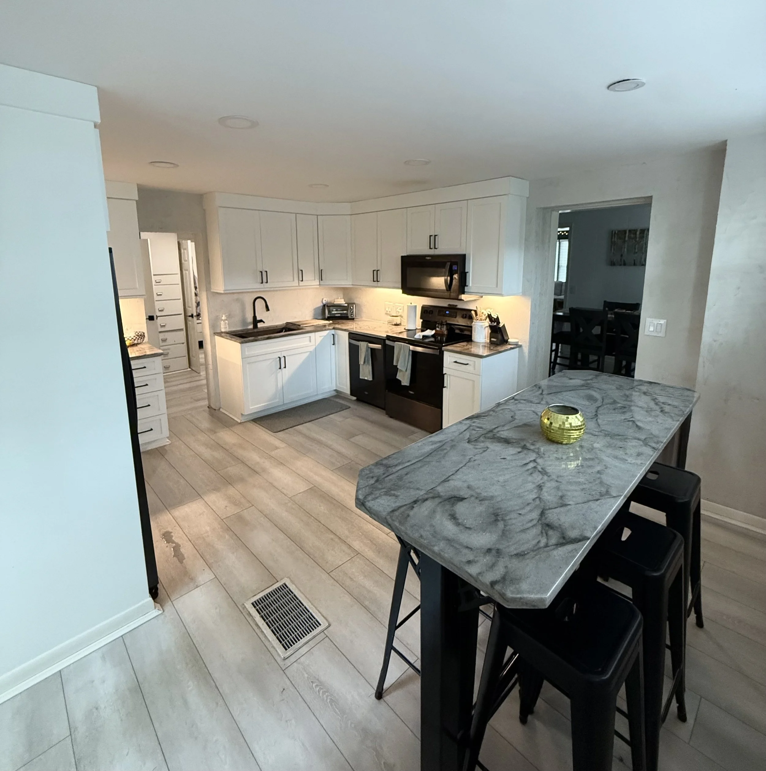 Kitchen with white cabinets, black appliances, marble countertop island, and black chairs at the breakfast bar.