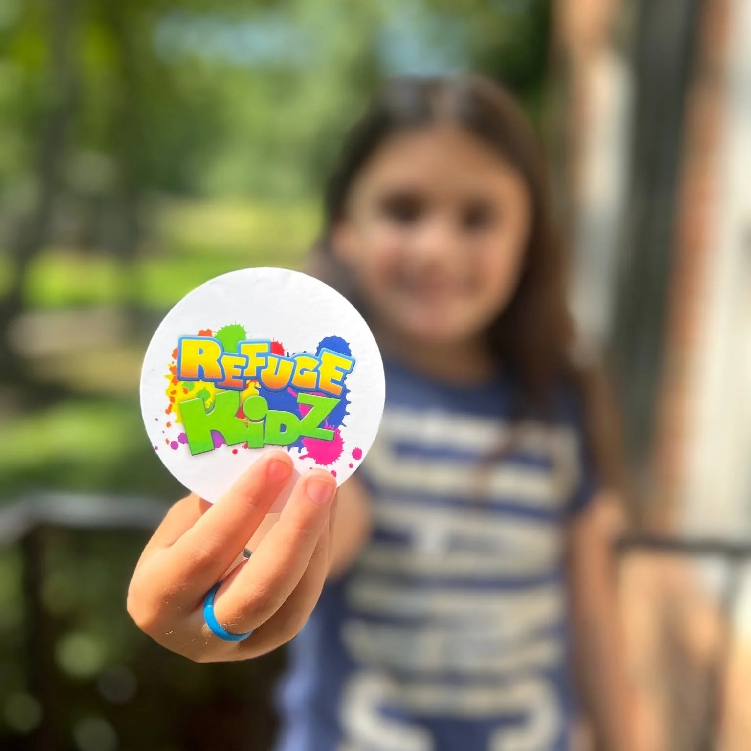 A child holding the Refuge Kids logo