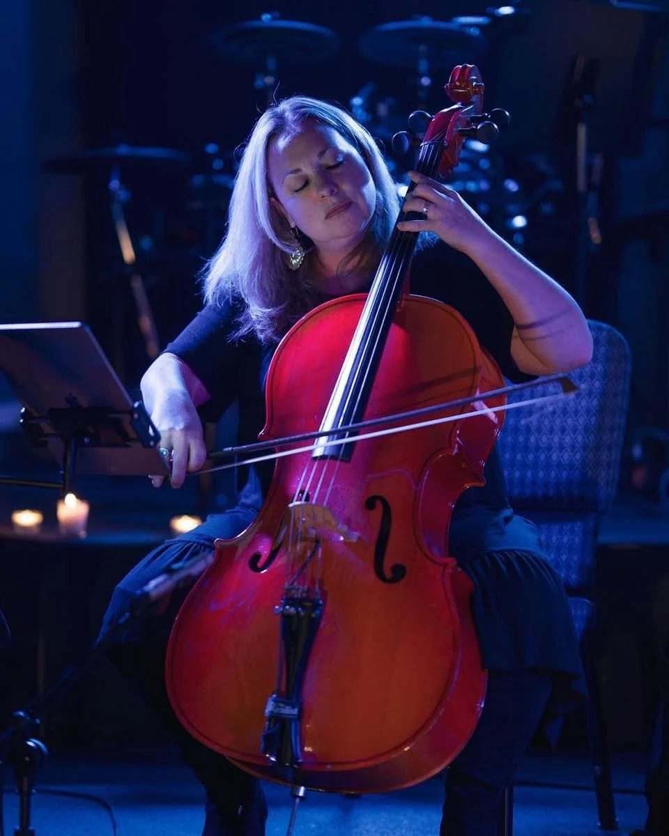 A woman playing a cello during a performance in a dimly lit venue.