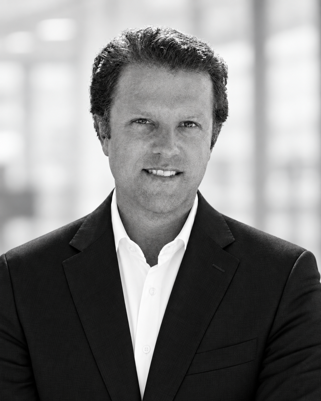 Black and white portrait of a middle-aged man with dark, curly hair, wearing a suit and white shirt, smiling slightly.