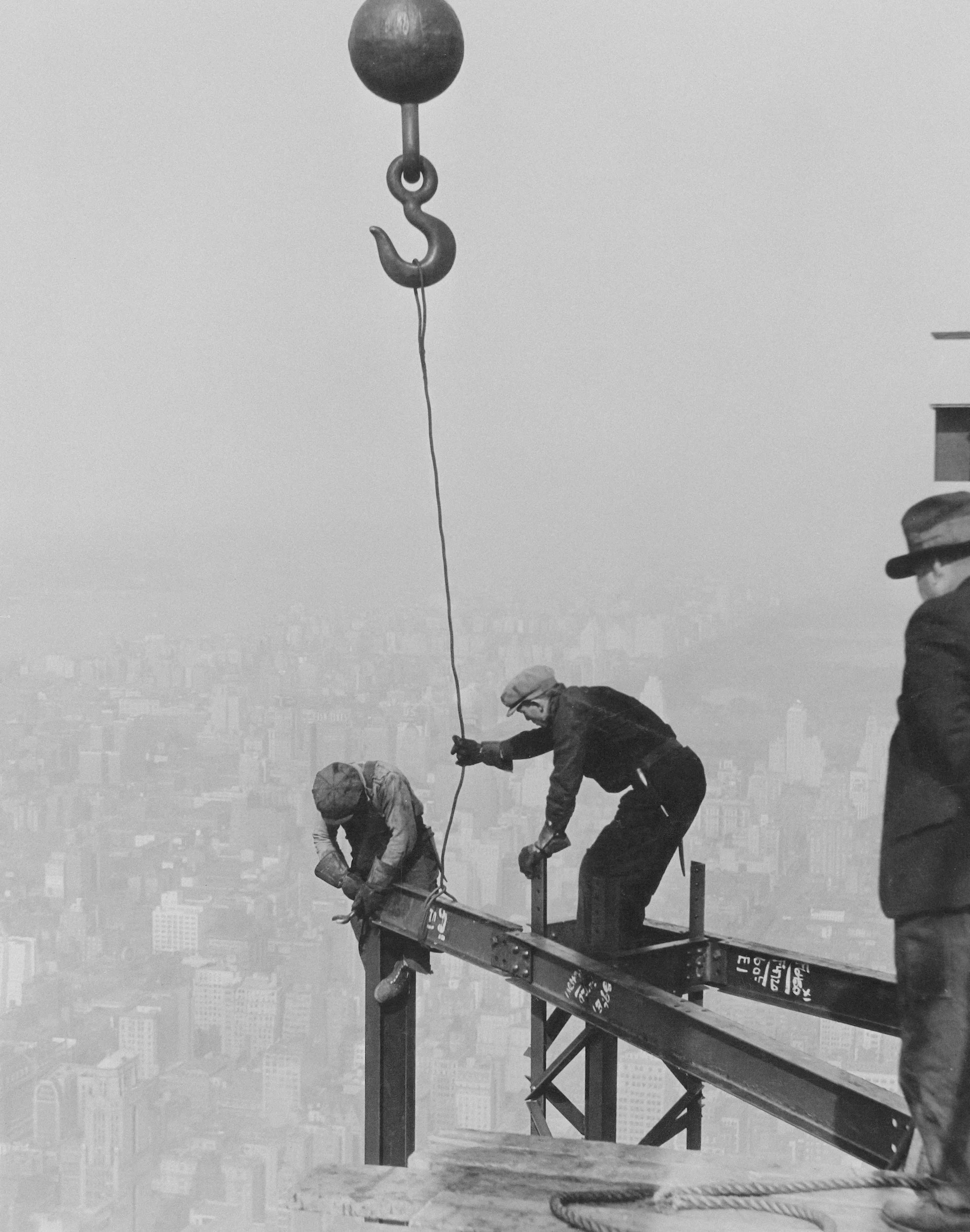 People working on the top of a tall building, installing or repairing a structure with a cityscape in the background.