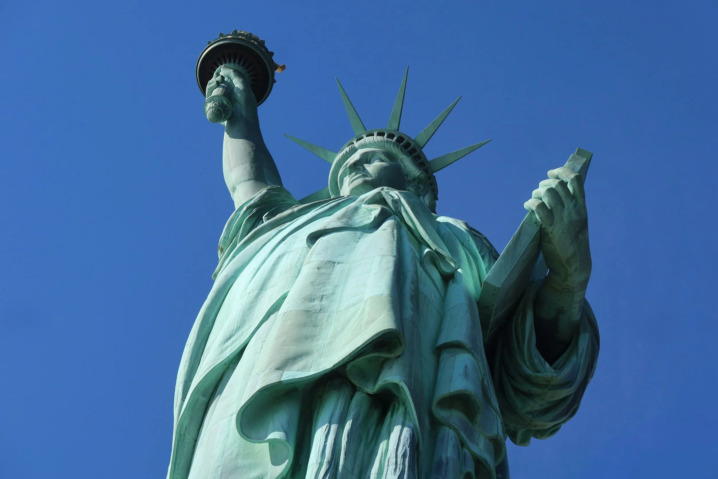 Close-up of the Statue of Liberty against a clear blue sky, showing her face, crown, and raised torch.
