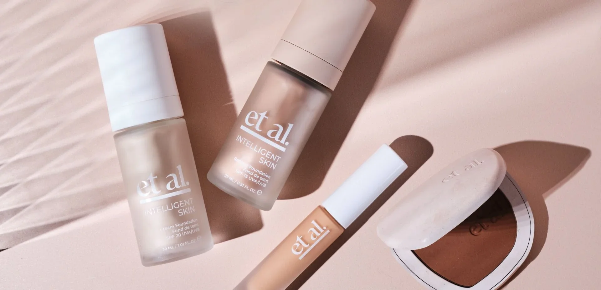 Arrangement of skincare and makeup products on a pink surface, including bottles labeled 'et al!', a tube, a compact, and a soap bar with a smooth, oval shape.