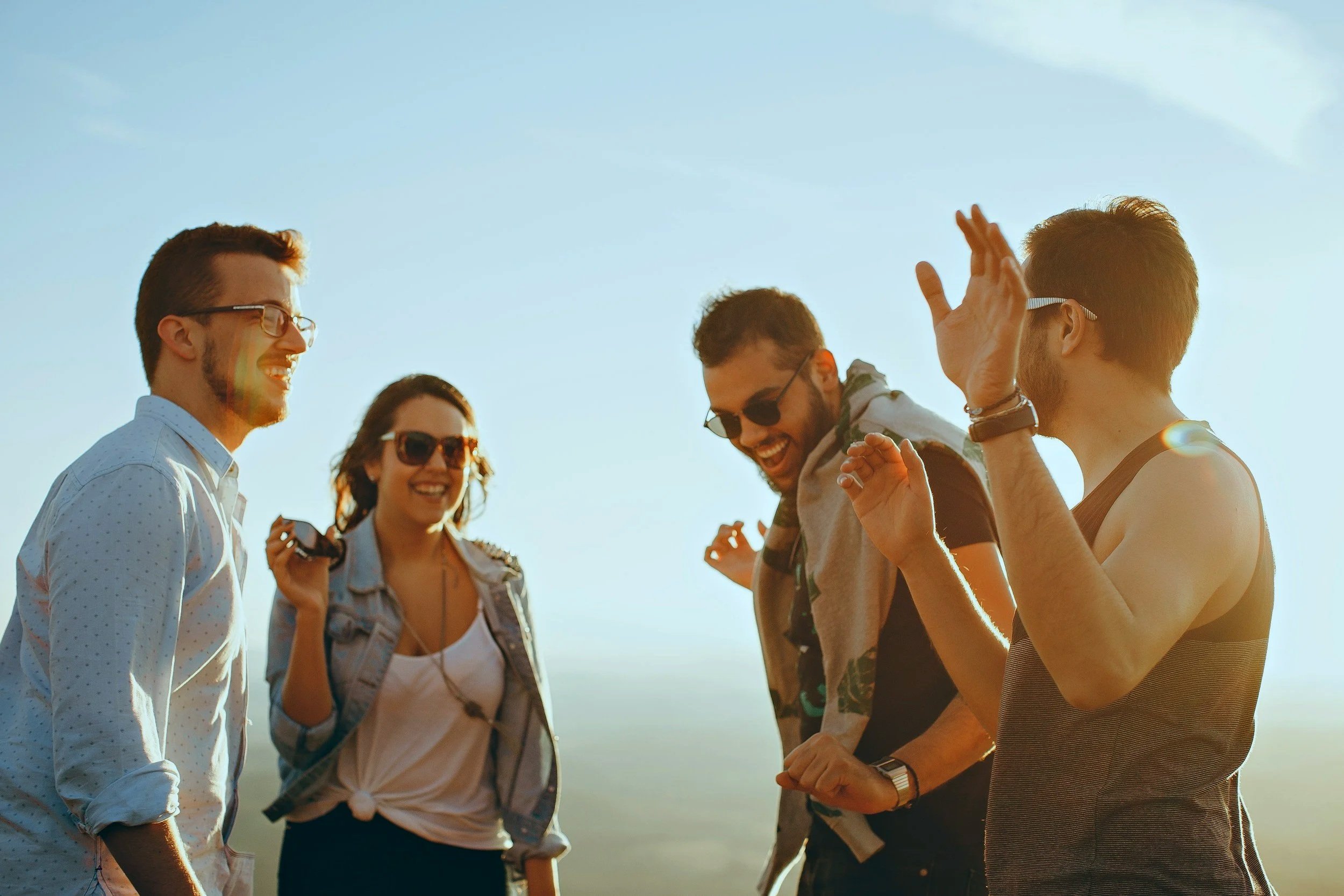 A group of five young adults smiling and talking outdoors during sunset, with clear blue sky in the background.