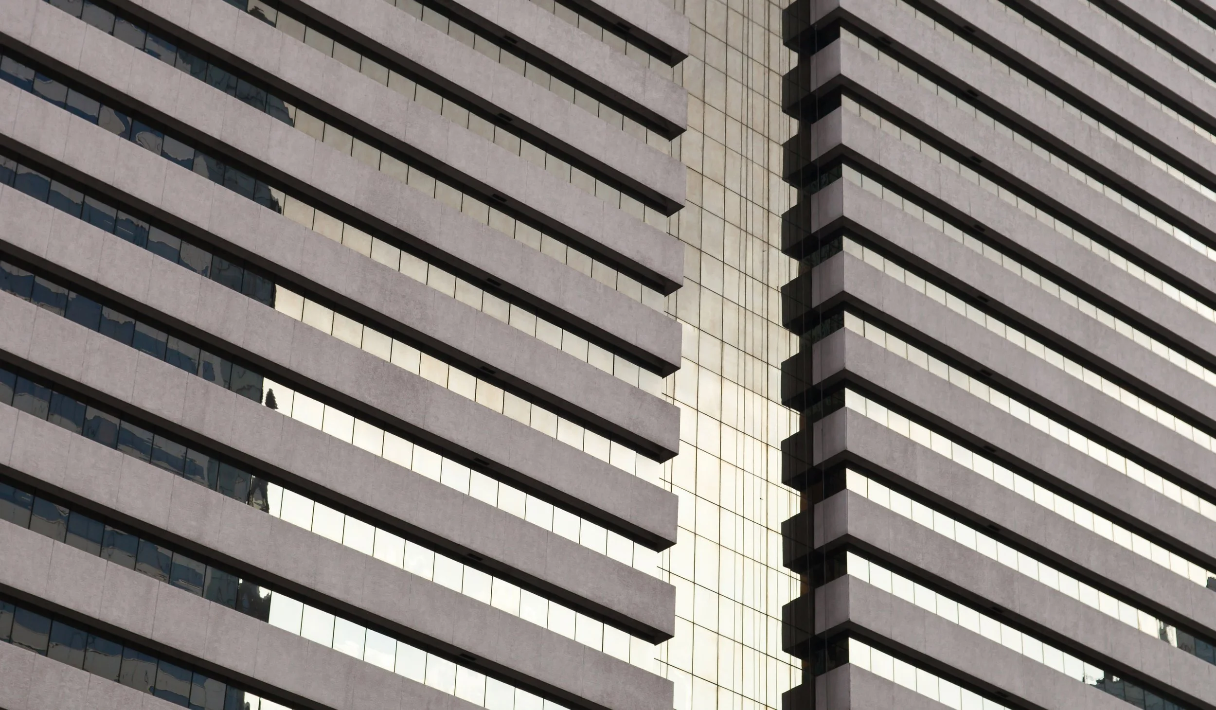 Close-up of a modern high-rise building with alternating beige concrete balconies and reflective glass windows.