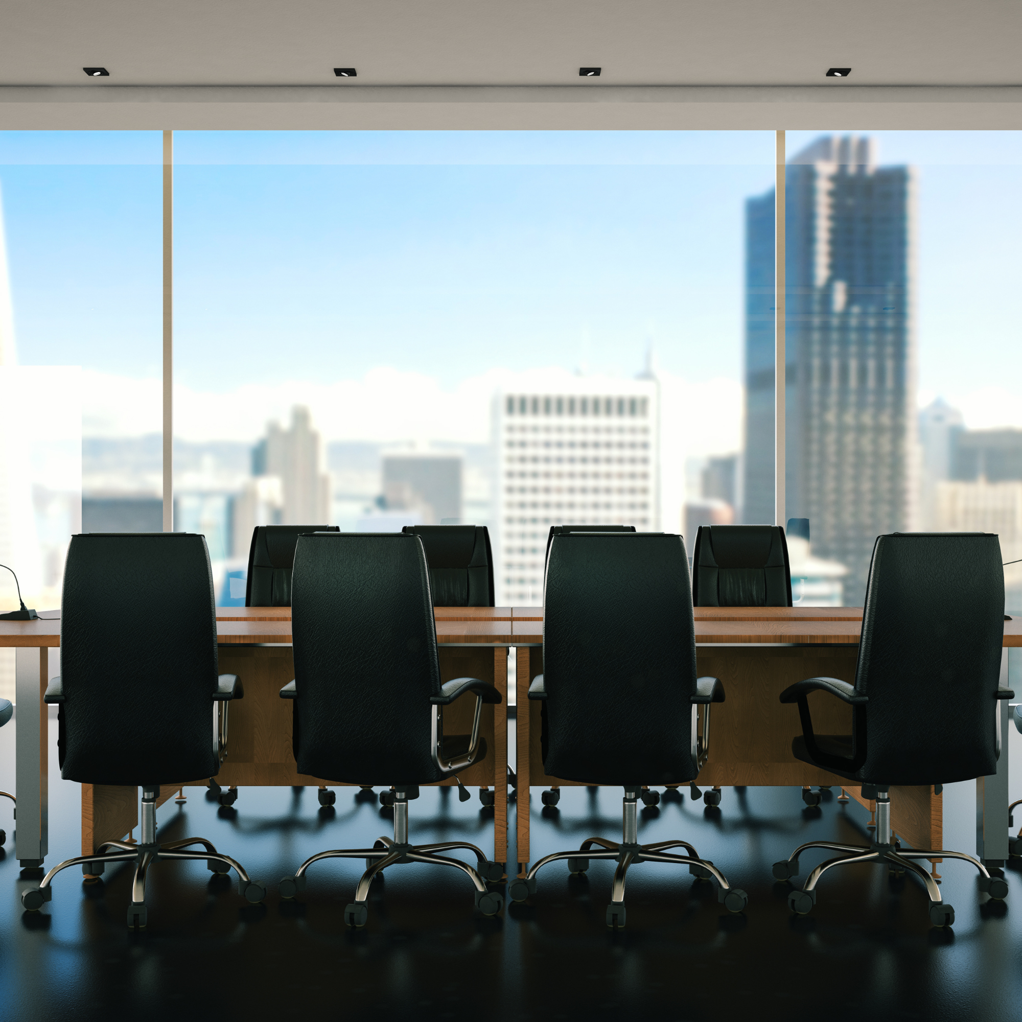 Empty conference room with black chairs around a wooden table, large windows with a city skyline view, and a ceiling with recessed lighting.