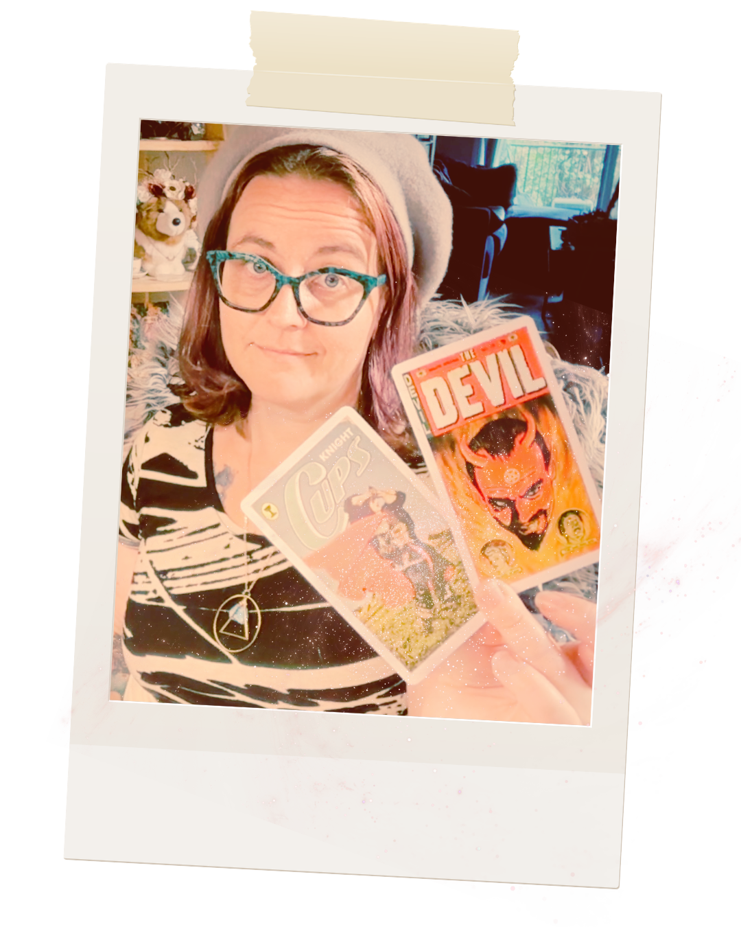 A person with glasses and a gray beret holding two trading cards, one titled "The Devil" with a fiery demon illustration and the other titled "Knight Cips" with a knight on a horse, sitting on a furry blanket in a cozy room.