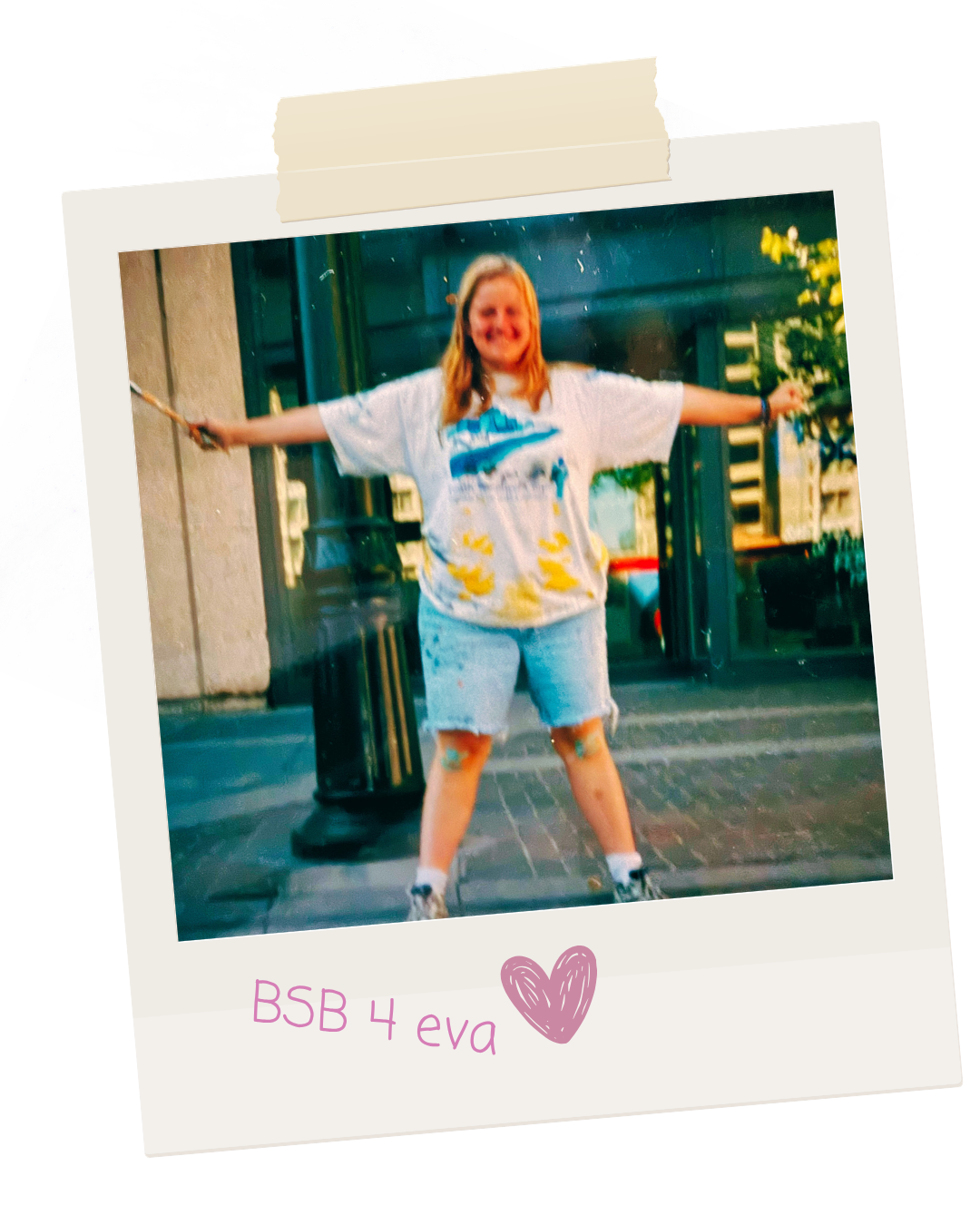 A young girl with long red hair standing outside on a sidewalk, holding a jump rope with arms outstretched, wearing a white t-shirt with a colorful design, denim shorts, and sneakers. Behind her are green doors and windows.