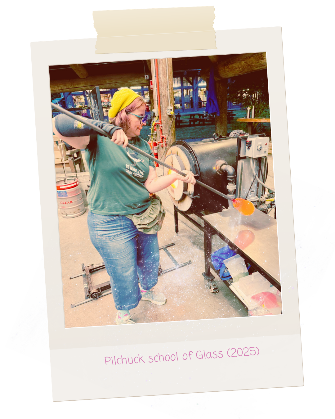 A woman with a yellow hat and glasses using a long metal rod to work on glass in a glassblowing studio. There are shelves, a table with tools, and a colorful outdoor background. Text on the photo reads 'Pilchuck School of Glass 2025'.