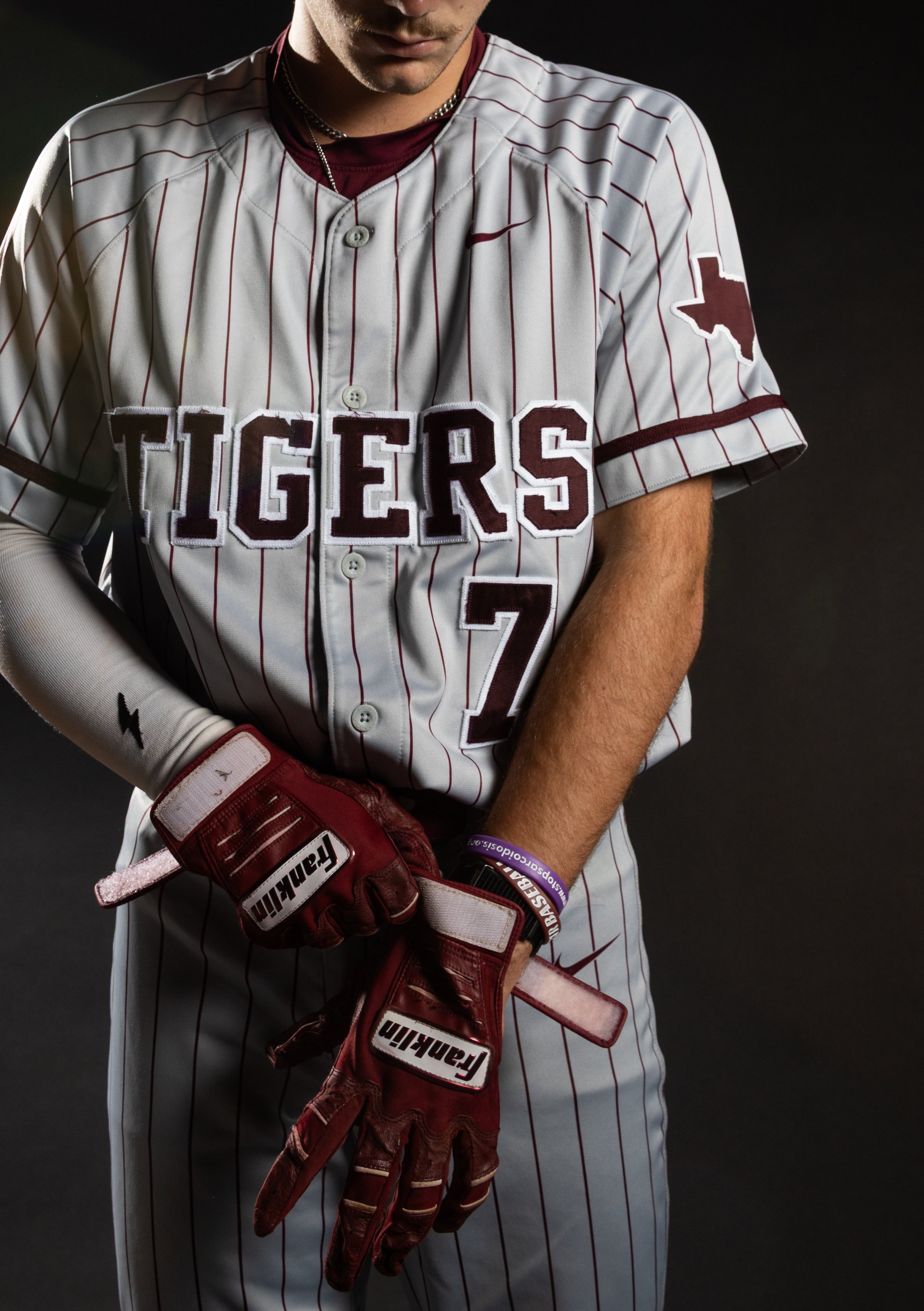 Close-up of a baseball player in uniform, holding a glove, with facial expression not fully visible, against a dark background