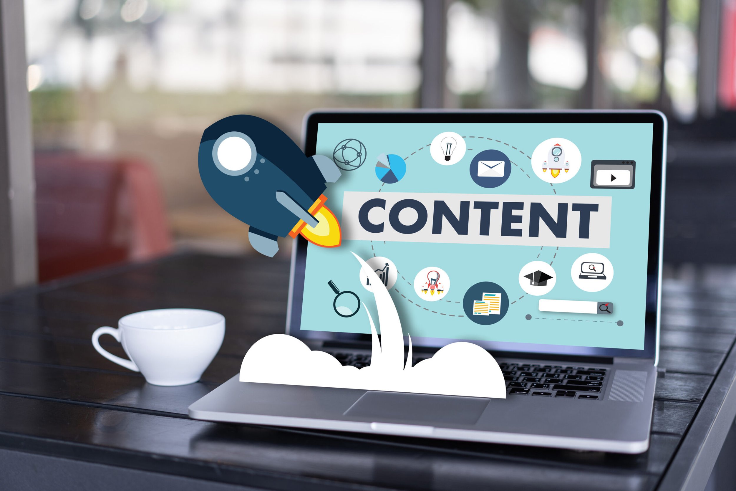 A laptop on a black table displays a graphic with the word 'CONTENT' and various icons related to ideas, communication, and analysis. A white coffee mug is beside the laptop, and a blurred background shows a window with natural light.
