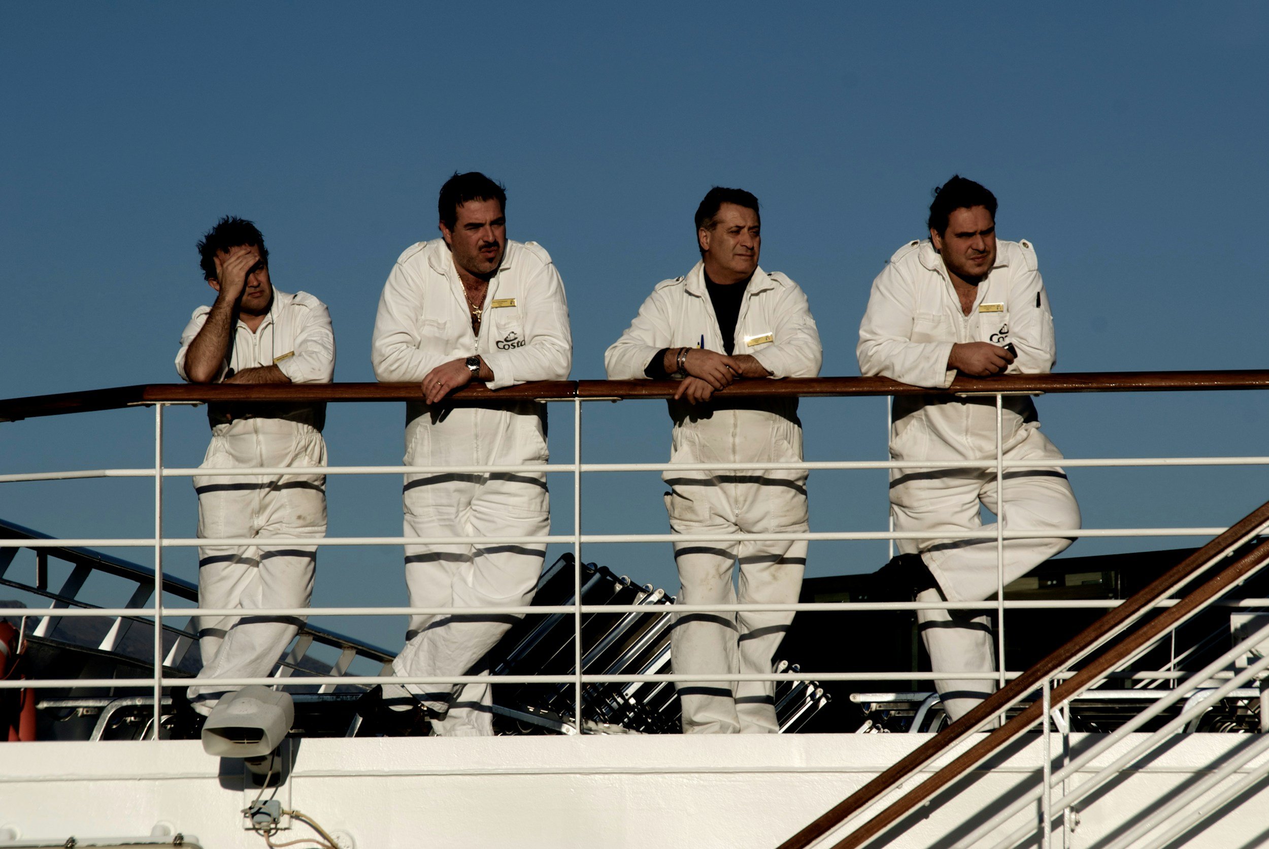 Four men in white uniforms standing on a ship's deck against a clear blue sky.