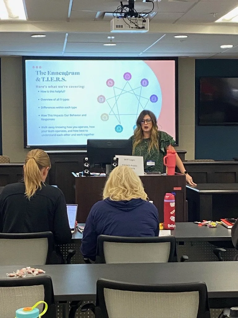 Alex Fittin gives a presentation on the Enneagram personality types to a small group in a conference room in Bentonville, Arkansas. The presentation slide displays a diagram of the Enneagram and information about its types.