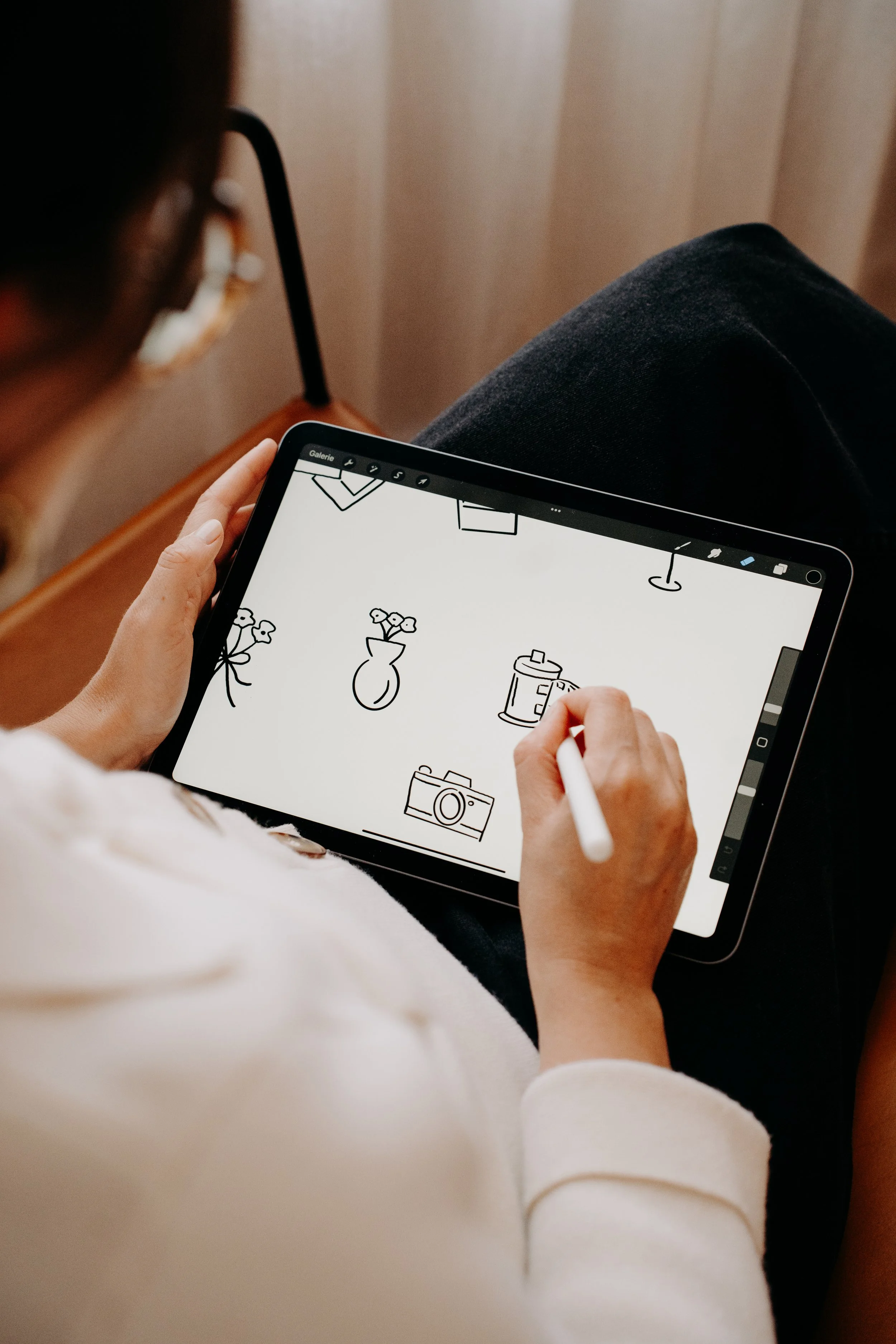 Personne dessinant des esquisses de différents objets sur une tablette, vue partielle.