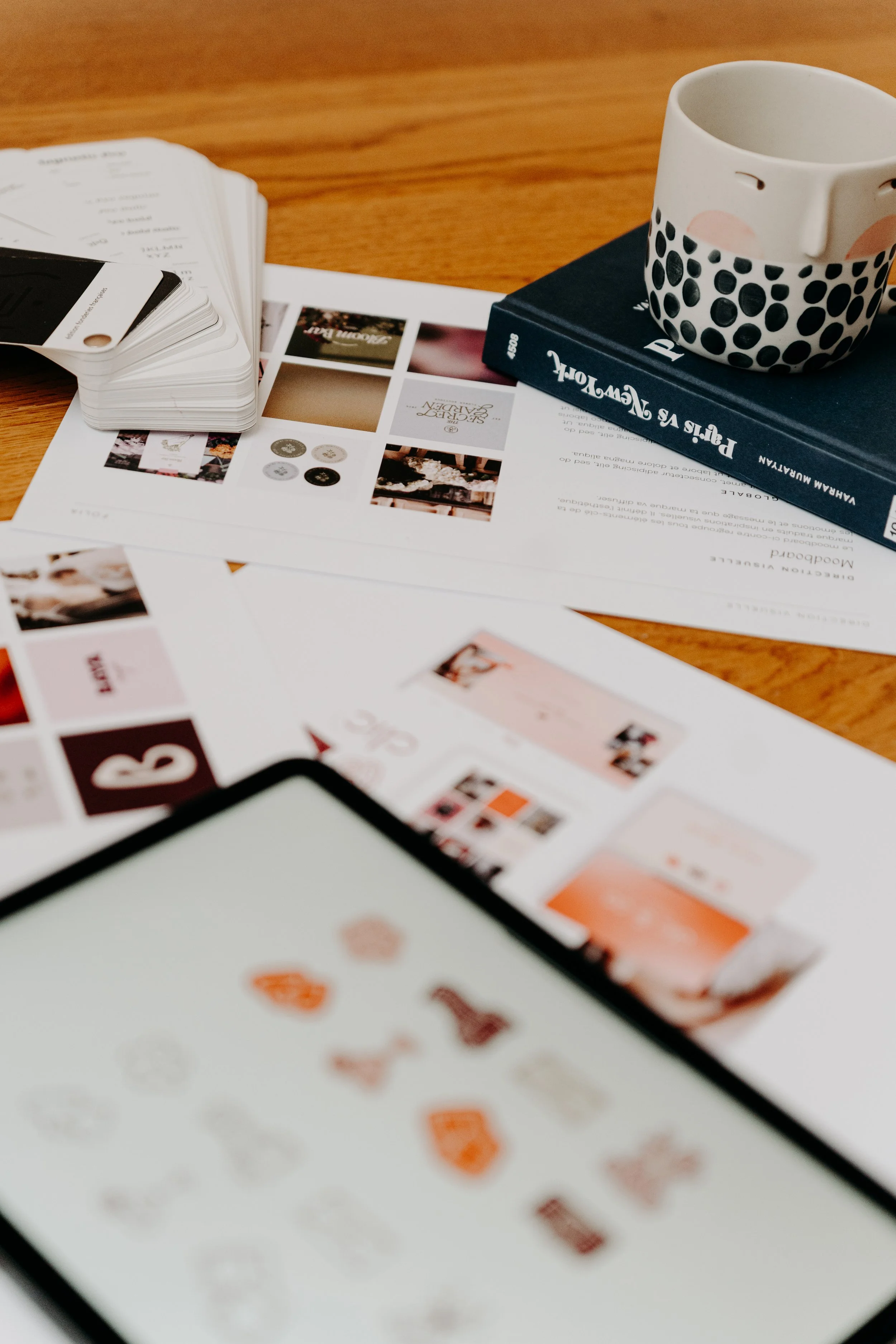 Vue d'un bureau avec un verre personnalisé avec un visage, un livre, une tablette et des papiers avec des images et du texte, tous sur une table en bois.