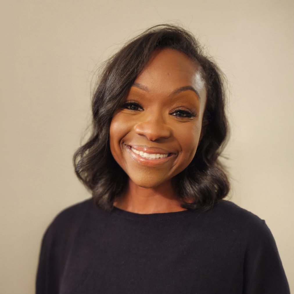 Close-up of a smiling African American woman with shoulder-length wavy black hair, wearing a black top, against a neutral background.