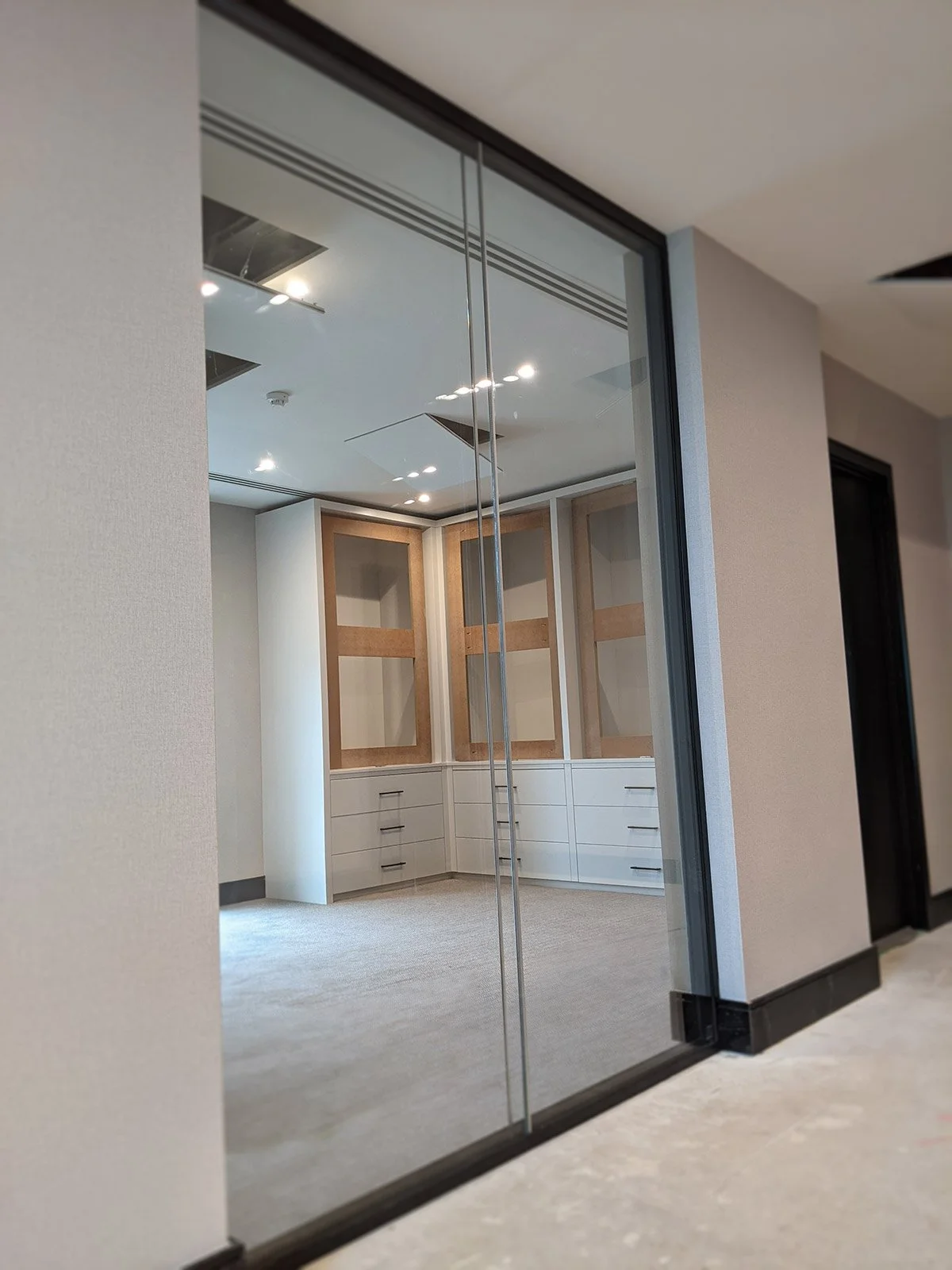 Interior view of a modern room with built-in cabinets and glass sliding doors, seen through a glass wall.