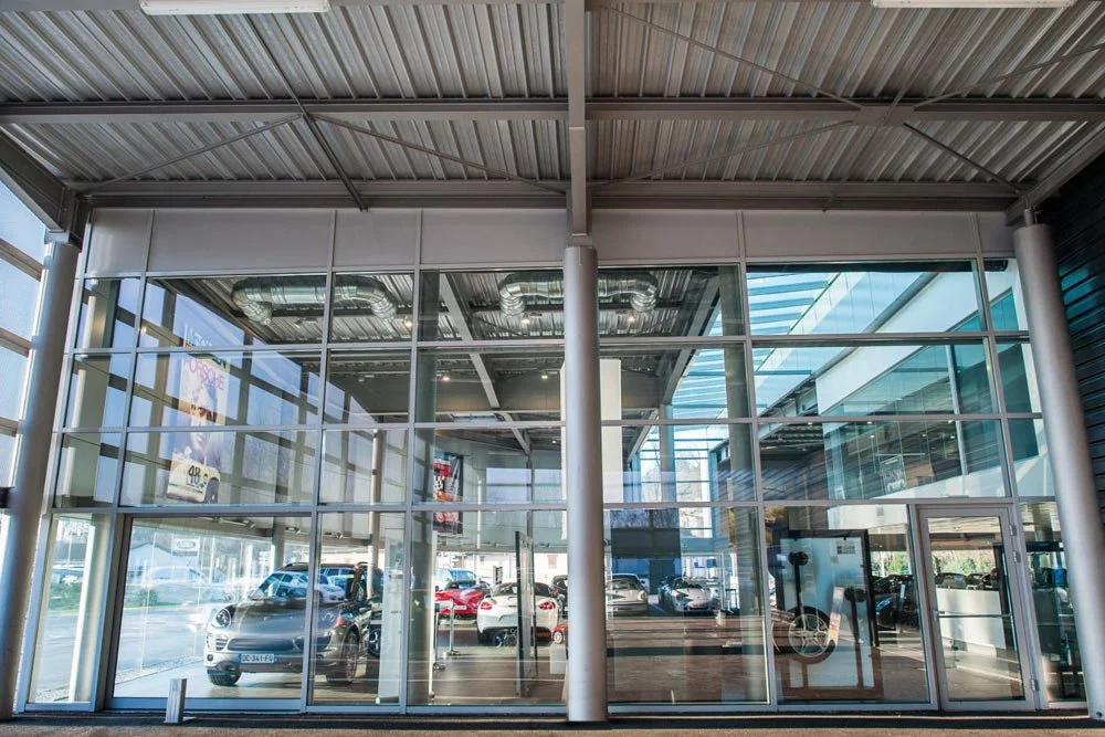 Exterior view of a modern car dealership with glass windows displaying various cars inside and outside