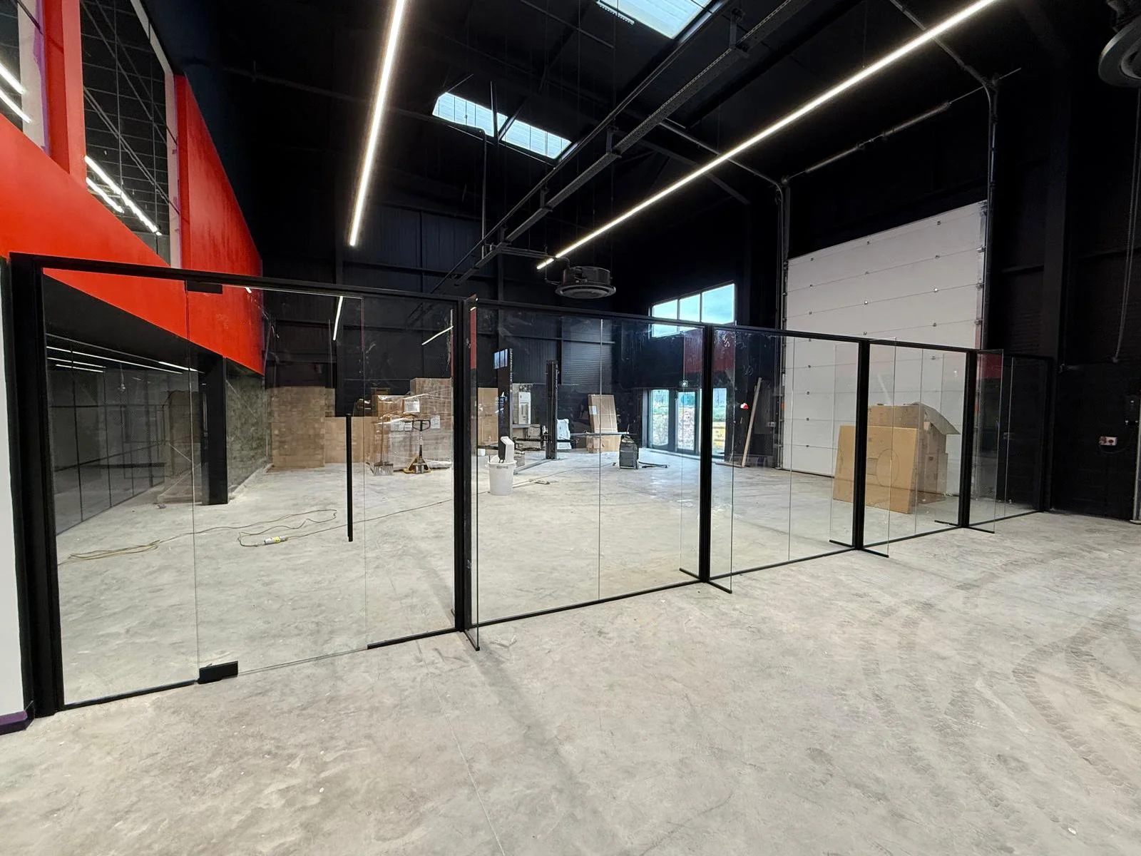 Interior of a commercial space under construction with a black ceiling, skylights, glass partitions, and construction materials scattered on the unfinished concrete floor.