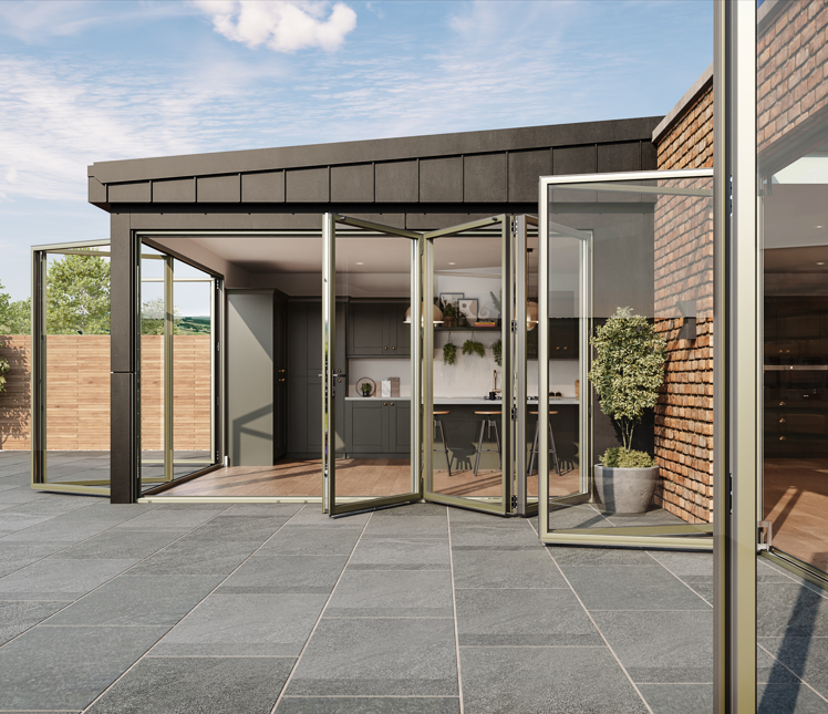 Modern patio with glass doors opening into a kitchen and dining area, brick and dark panel exterior, wooden fence, tiled ground, potted plant, outdoors with blue sky.