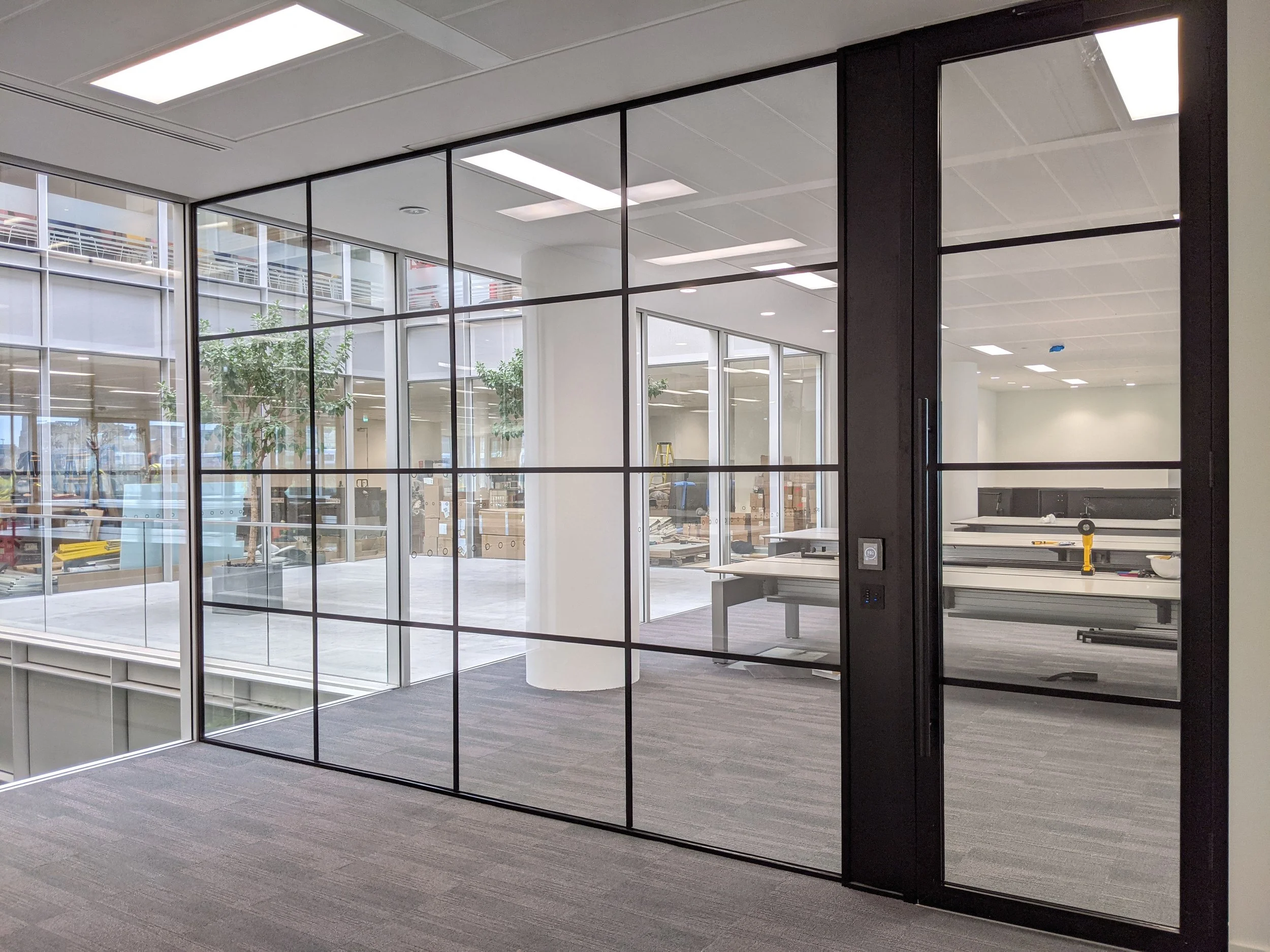 Interior view of an office space with glass walls, visible desks, and ceiling lights.
