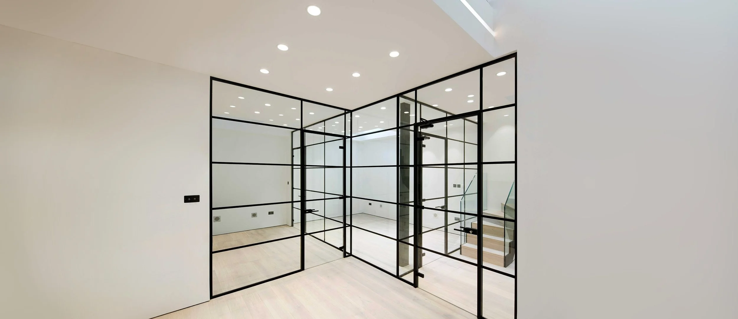 Modern interior with white walls, a black metal-framed glass partition, and recessed ceiling lights.