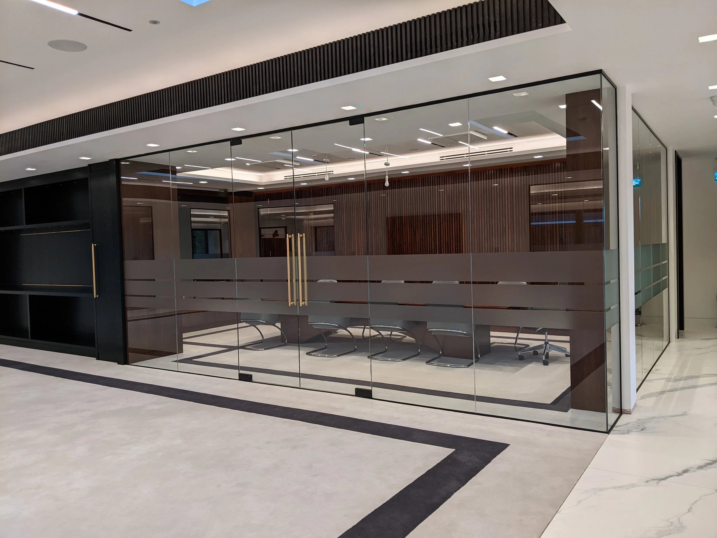 A modern building entrance with glass doors and walls, black accents, and a sleek interior design with wood and metal details.