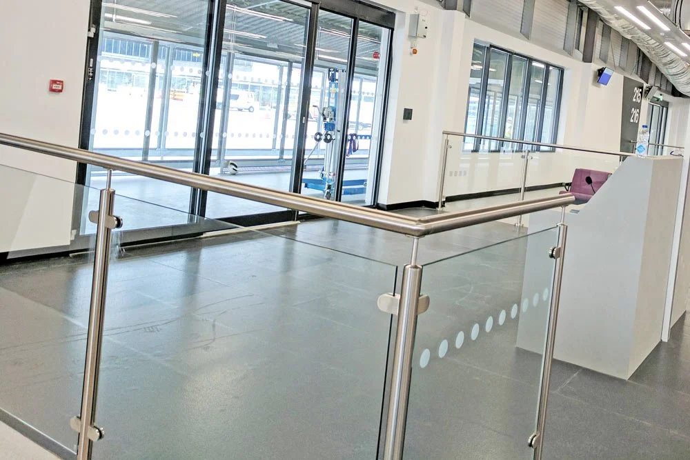 Empty airport terminal with a glass entrance and metal railings.