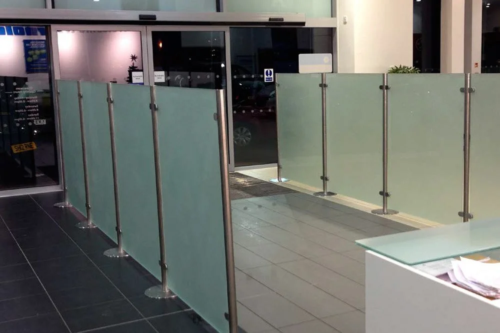 Indoor area with glass barrier panels, possibly an entrance or exit, with a tiled floor and a glass door leading outside at night.