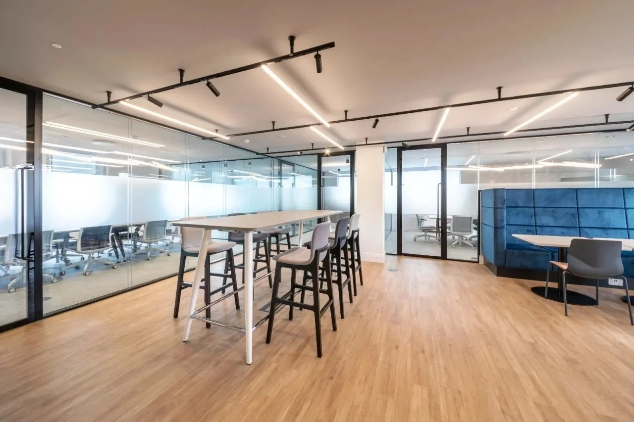 Modern office space with high-top tables, chairs, a blue booth, and a glass-walled conference room.