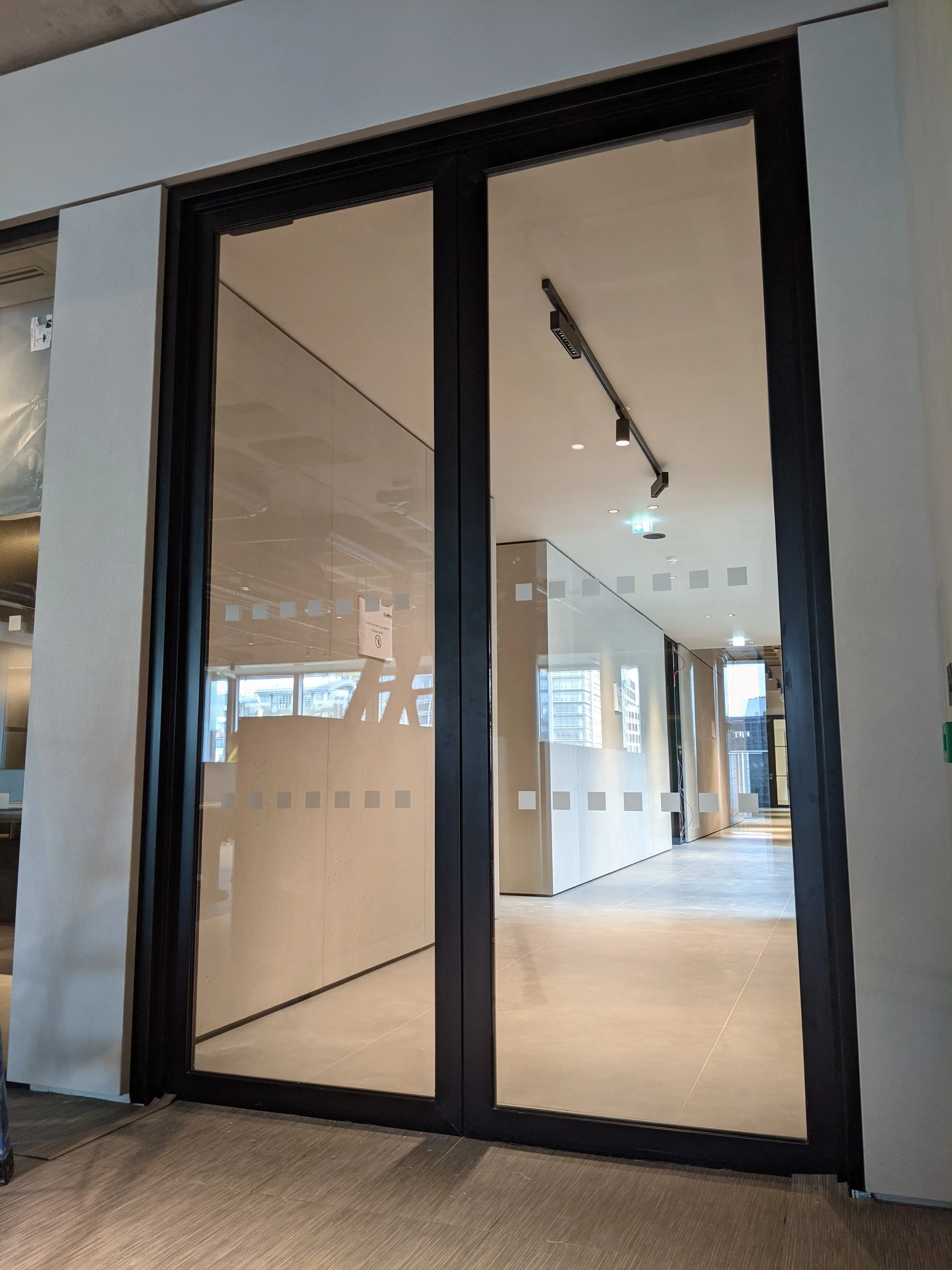 A large glass sliding door with a black frame leading into a modern interior space with beige walls, a light-colored tile floor, and city views outside.
