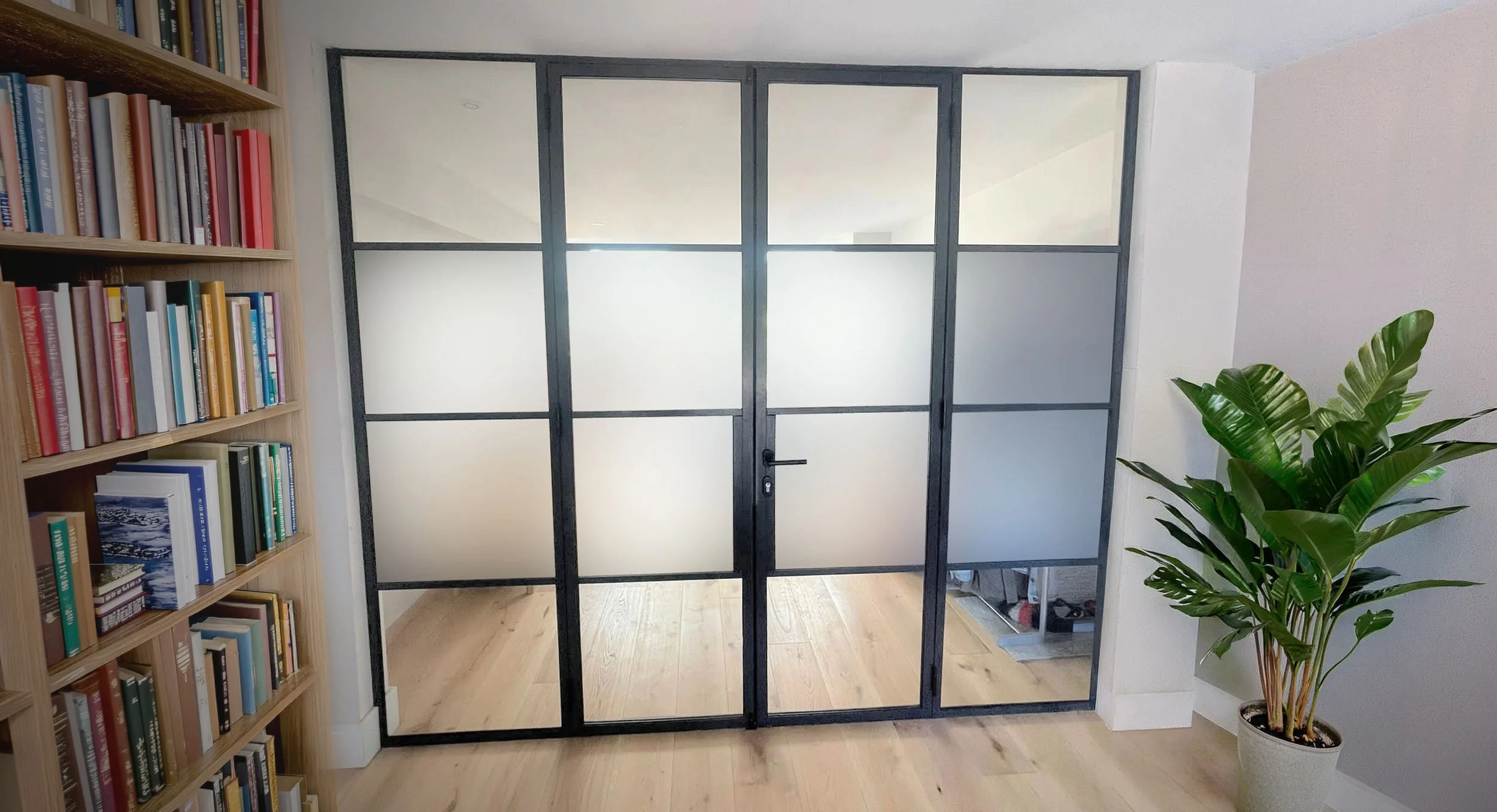 A black-framed frosted glass partition door in a room with a wooden bookshelf on the left and a green potted plant on the right.