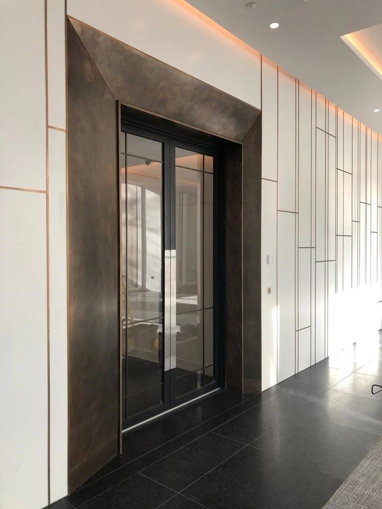 Modern elevator door with black glass and metallic frame in a sleek, contemporary interior space with decorative wall panels and black flooring.