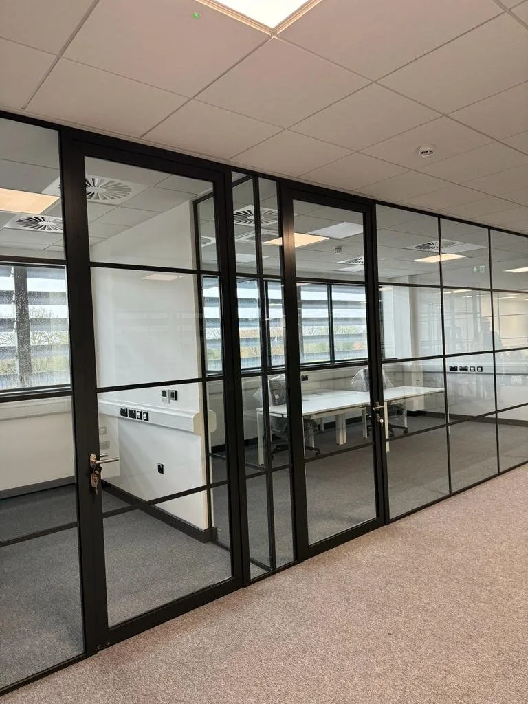 Modern office conference room with glass walls, white tables, black chairs, and large windows