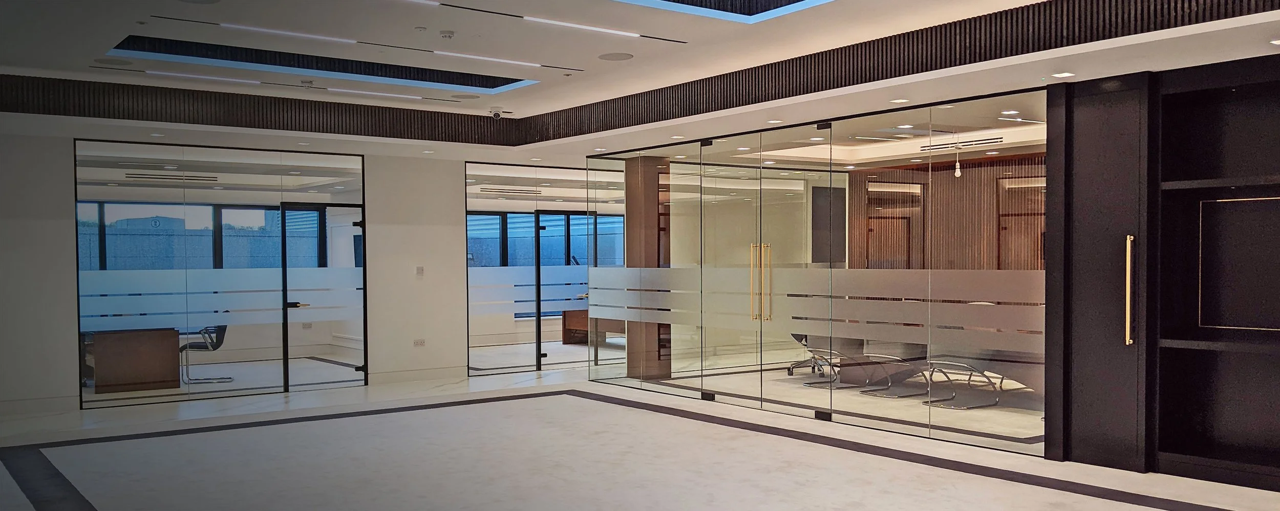 Modern office space with glass partitions, waiting area with chairs, and conference room with desk and chairs.