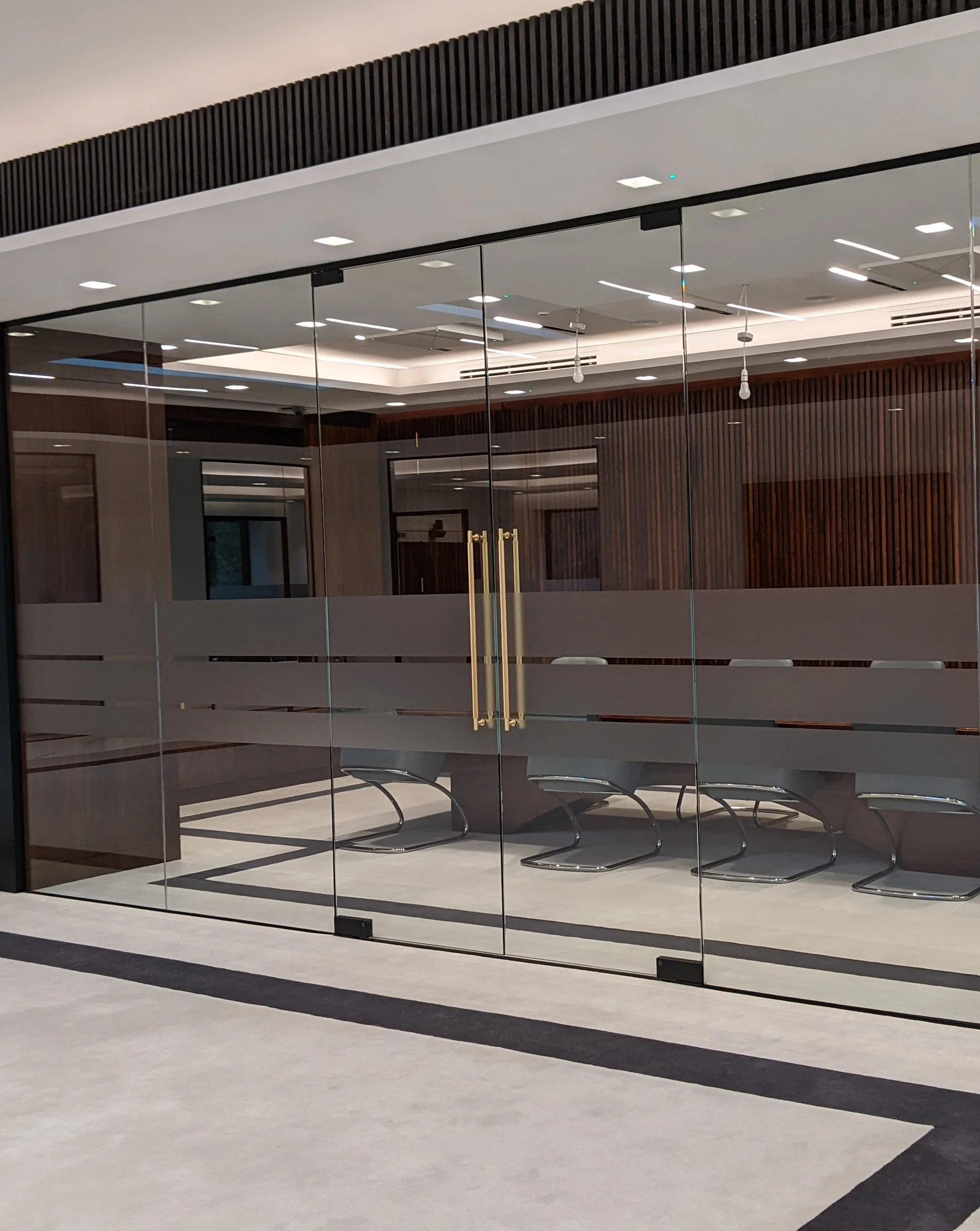 Modern conference room with glass doors, wooden walls, lounge chairs, and ceiling lights.