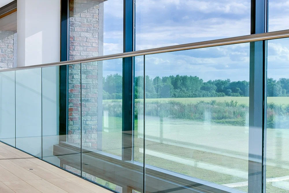 Interior view of a modern building with large glass windows showing a grassy field and trees outside.